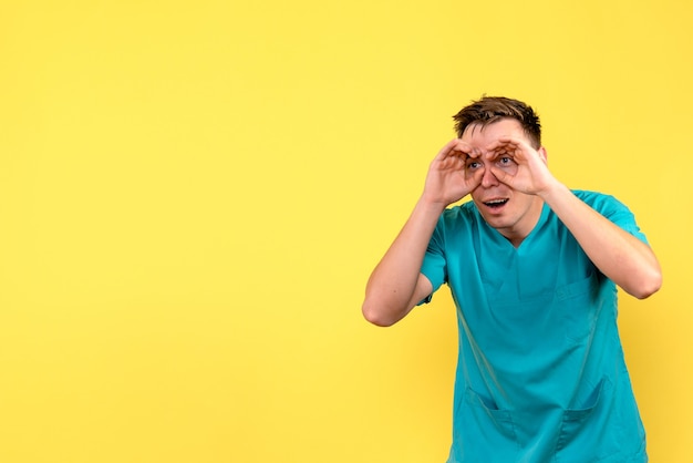 Front view of male doctor looking through fingers on yellow wall