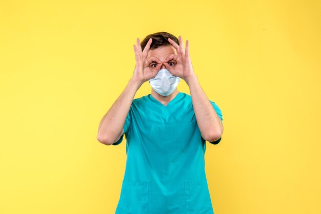 Front view of male doctor looking through fingers on yellow wall