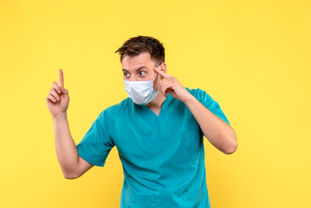 Вид спереди мужчины-врача в маске на светло-желтой стене