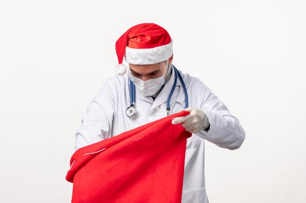 Front view of male doctor in mask with present bag on white wall