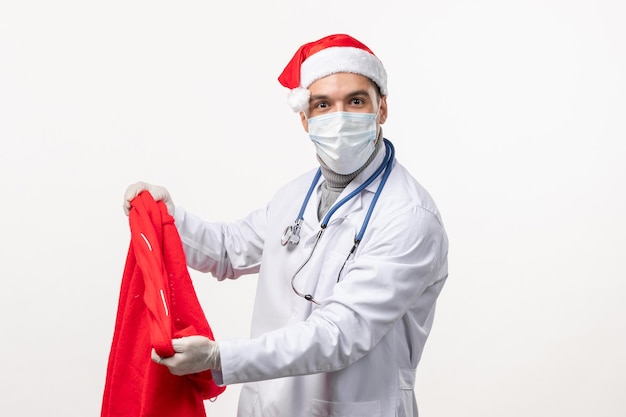 Front view of male doctor in mask with present bag on white wall