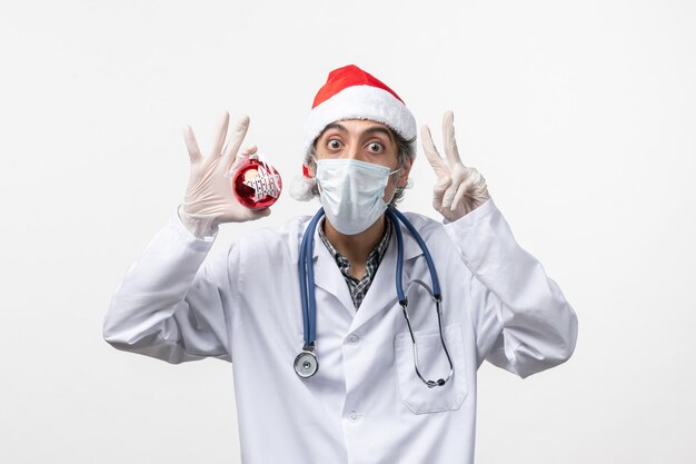 Front view male doctor in mask with toy on a white wall health virus covid new year