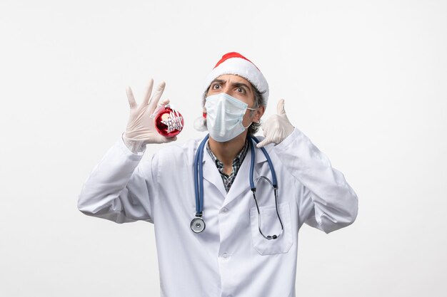 Front view male doctor in mask with toy on the white wall health virus covid new year