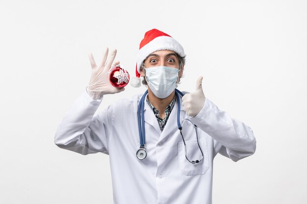 Front view male doctor in mask with toy on white wall health virus covid new year