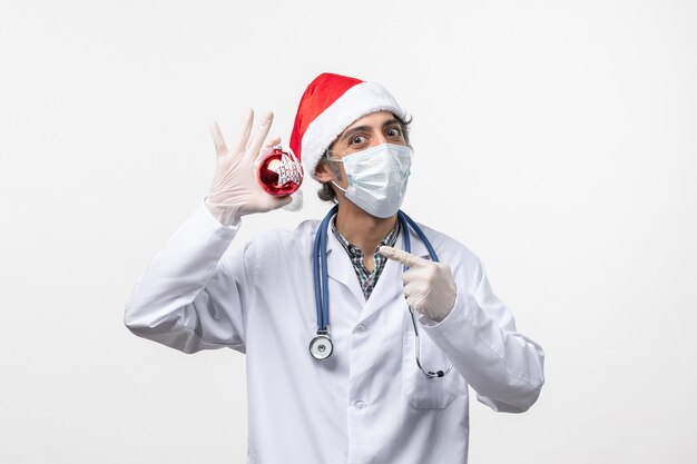 Front view male doctor in mask with toy on the white wall virus covid health new year