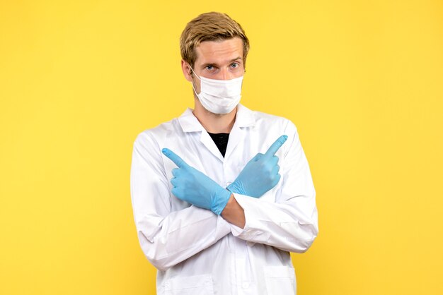 Front view male doctor in mask on a yellow background covid- health pandemic medic