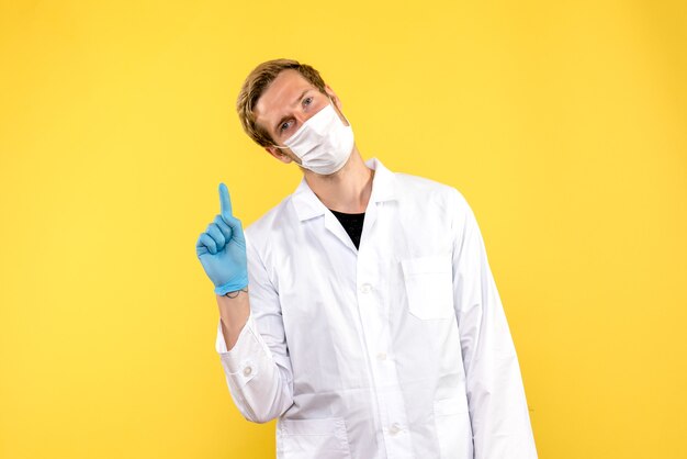 Front view male doctor in mask on a yellow background health covid- medic pandemic