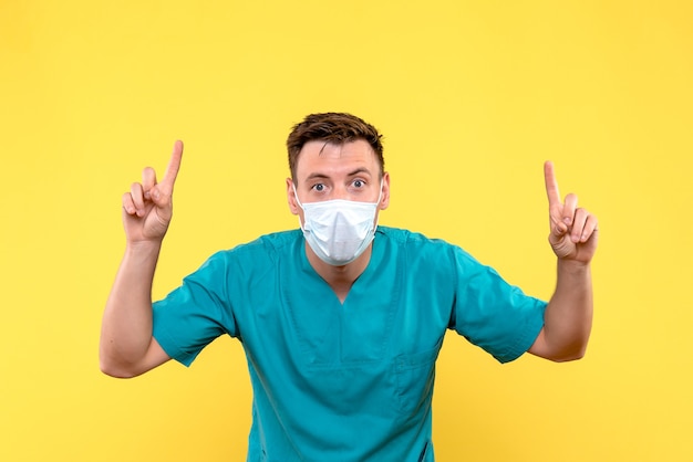 Front view of male doctor in mask on a yellow wall