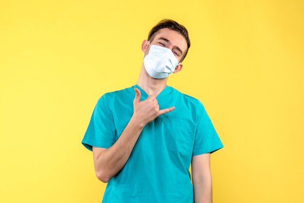 Front view of male doctor in mask on a yellow wall