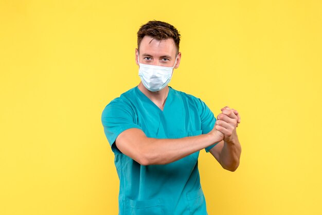 Front view of male doctor in mask on a yellow wall