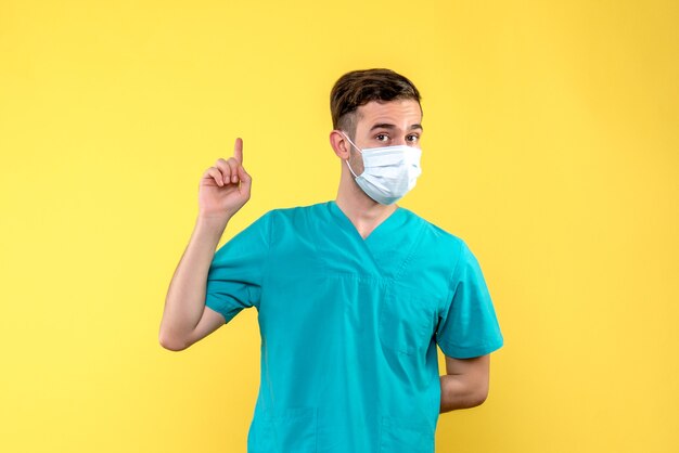 Front view of male doctor in mask on a yellow wall