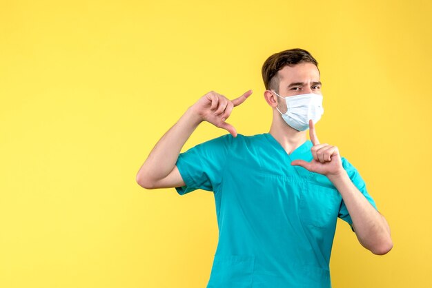 Front view of male doctor in mask on yellow wall