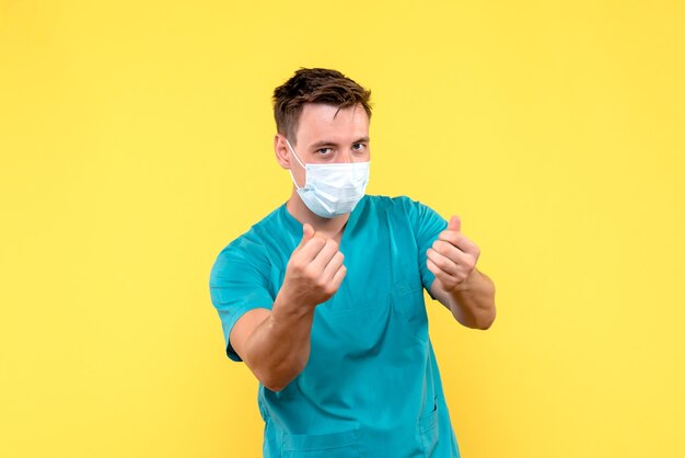 Front view of male doctor in mask on yellow wall