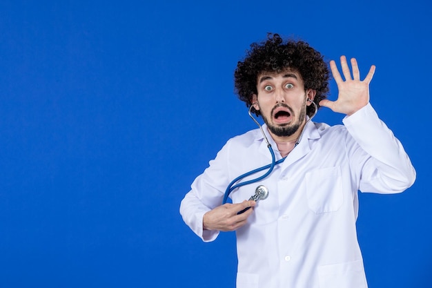 Вид спереди врача-мужчины в медицинском костюме, проверяющего свое тело стетоскопом на синем фоне, вакцины, пандемического препарата, ковидной больницы