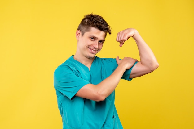 Front view of male doctor in medical suit flexing on yellow wall