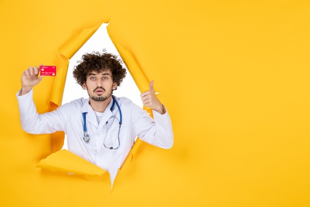 Front view male doctor in medical suit holding bank card on yellow color hospital disease health virus medic