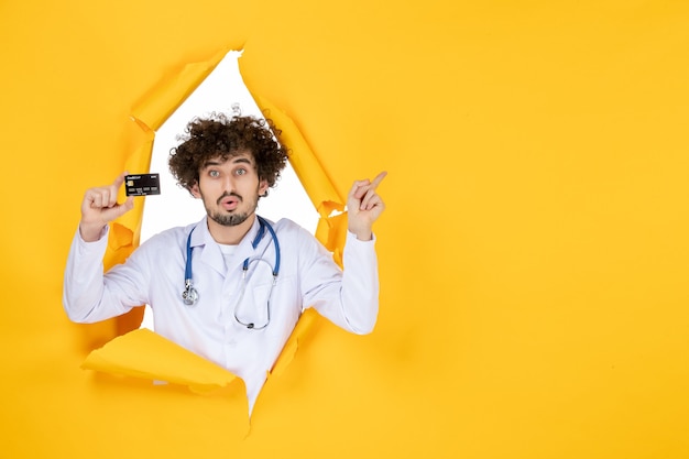 Вид спереди мужчина-врач в медицинском костюме, держащий банковскую карту на желтом разорванном цвете, медик, здоровье, медицина, больничная болезнь