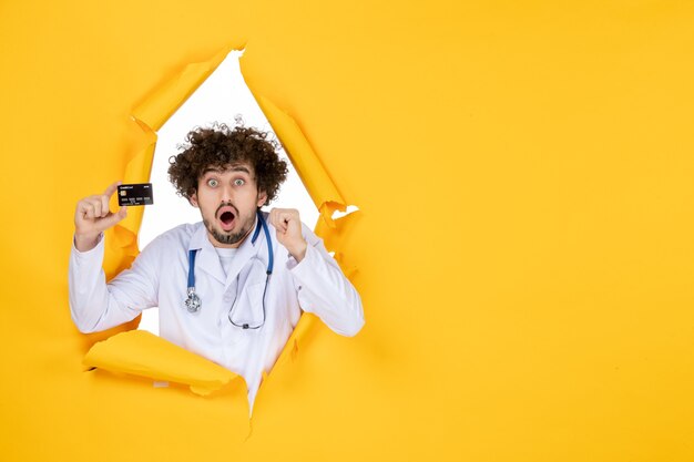 Free photo front view male doctor in medical suit holding bank card on a yellow ripped color medic medicine hospital disease health virus