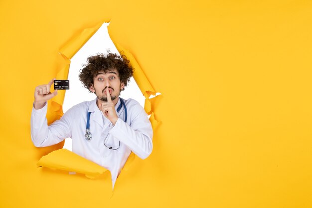 Free photo front view male doctor in medical suit holding bank card on yellow ripped color medic medicine hospital disease health virus