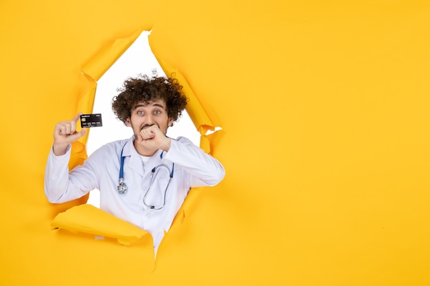 Free photo front view male doctor in medical suit holding bank card on yellow ripped color medic medicine virus hospital disease health