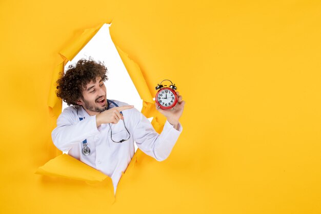 Front view male doctor in medical suit holding clocks on yellow health color shopping medicine time medic