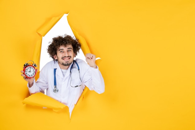 Front view male doctor in medical suit holding clocks on yellow medicine color health time hospital virus
