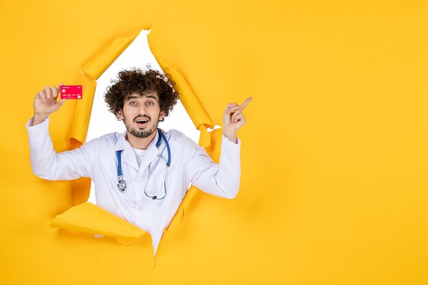 Front view male doctor in medical suit holding red bank card on yellow color medicine hospital disease health virus medic