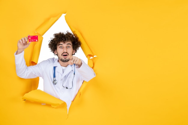 Вид спереди мужчина-врач в медицинском костюме, держащий красную банковскую карту на желтом цвете, медицина, больничная болезнь, вирус, здоровье, медик