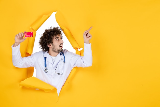 Foto gratuita vista frontale medico maschio in tuta medica con carta di credito rossa su colore giallo medicina ospedale malattia virus medico soldi salute