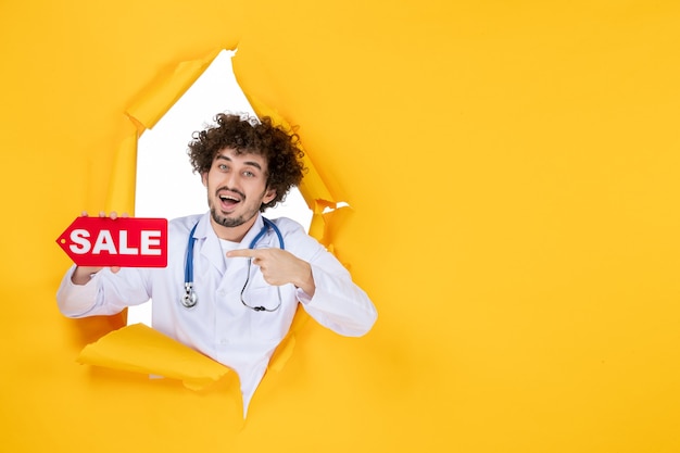 Вид спереди мужчина-врач в медицинском костюме, держащий красную распродажу, пишущий на желтом медике, здоровье, болезнь, больничная медицина