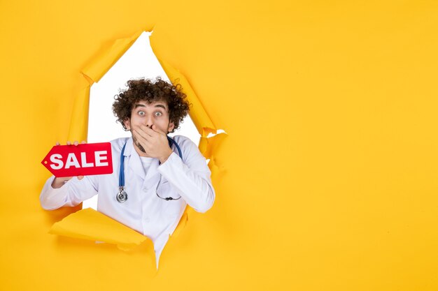 Вид спереди мужчина-врач в медицинском костюме держит красную распродажу с надписью на желтом медике.