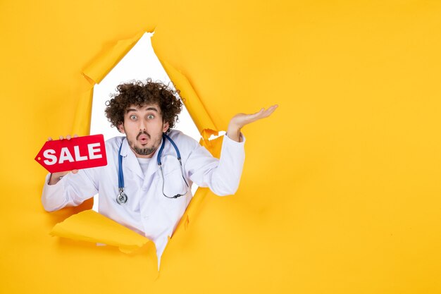 Front view male doctor in medical suit holding sale writing on the yellow color shopping medic health hospital medicine