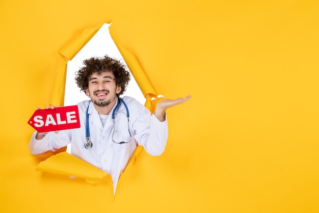 Вид спереди мужской доктор в медицинском костюме, держащий распродажу, пишущий на желтом торговом медике, цветная медицина