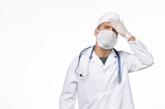 흰 벽에 그의 온도를 확인하는 코로나 바이러스에 대한 의료 소송 및 마스크의 전면보기 남성 의사 covid-virus 질병 질병 격리 전염병