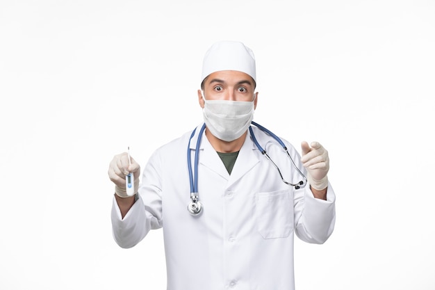 医療スーツを着た正面図の男性医師と、白い壁のウイルス感染症のパンデミックでのコロナウイルス保持装置に対するマスク