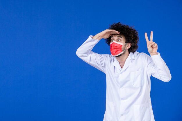 Front view of male doctor in medical suit and mask on blue background vaccine health drug hospital covid- coronavirus pandemic medicine