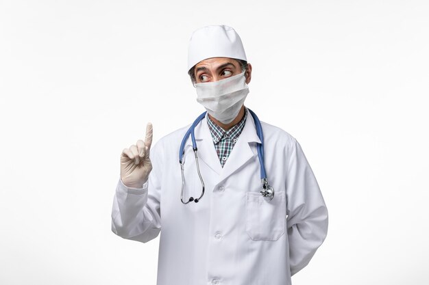 Вид спереди мужчина-врач в медицинском костюме и маске из-за коронавируса на белом столе