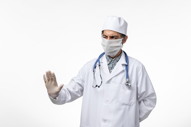 Front view male doctor in medical suit and mask due to coronavirus on the white surface