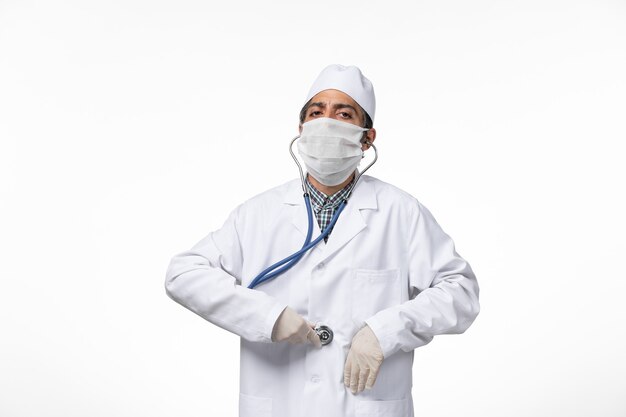 白い表面のコロナウイルスによる医療スーツとマスクの正面図男性医師