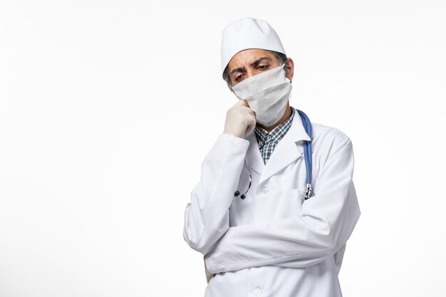 Front view male doctor in medical suit and mask due to coronavirus on white surface