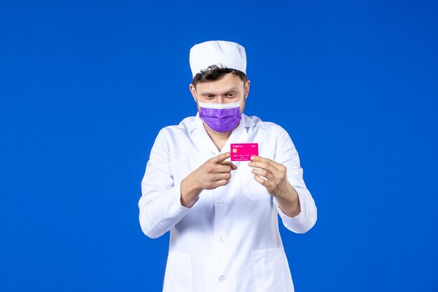 Вид спереди мужчины-врача в медицинском костюме и маске, держащего кредитную карту на синем
