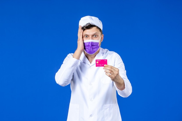 Free photo front view of male doctor in medical suit and mask holding credit card on blue