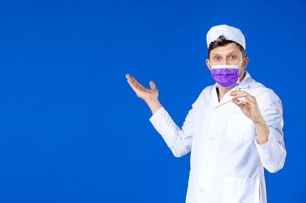 青に注射を保持している医療スーツとマスクの男性医師の正面図
