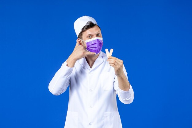 Front view of male doctor in medical suit and mask holding little medical patches on blue 