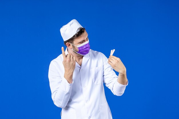 Front view of male doctor in medical suit and mask holding little medical patches on blue 