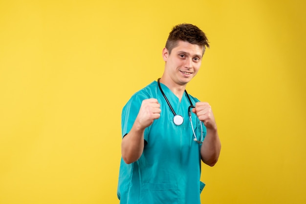 Front view of male doctor in medical suit posing on yellow wall