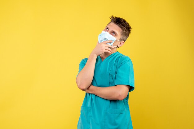 Вид спереди мужчины-врача в медицинском костюме и защитной маске, думая на желтой стене