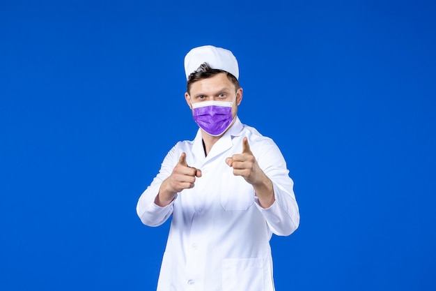 Vista frontale del medico maschio in tuta medica e maschera viola sull'azzurro