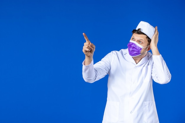 Front view of male doctor in medical suit and purple mask on blue 