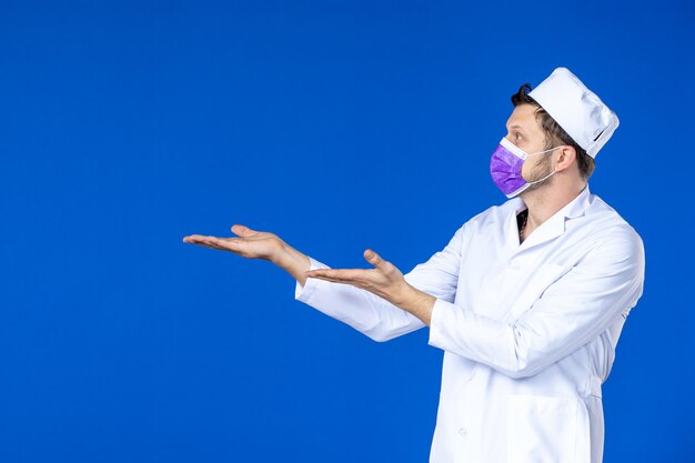 Front view of male doctor in medical suit and purple mask on blue 